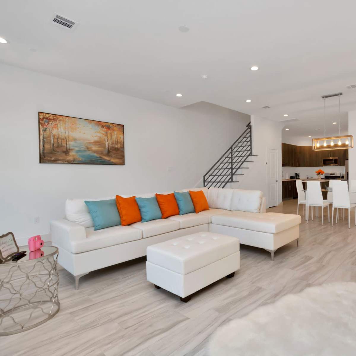 A modern living room featuring a white sectional sofa with orange pillows, a coffee table, and a dining area with a wooden table and chairs.