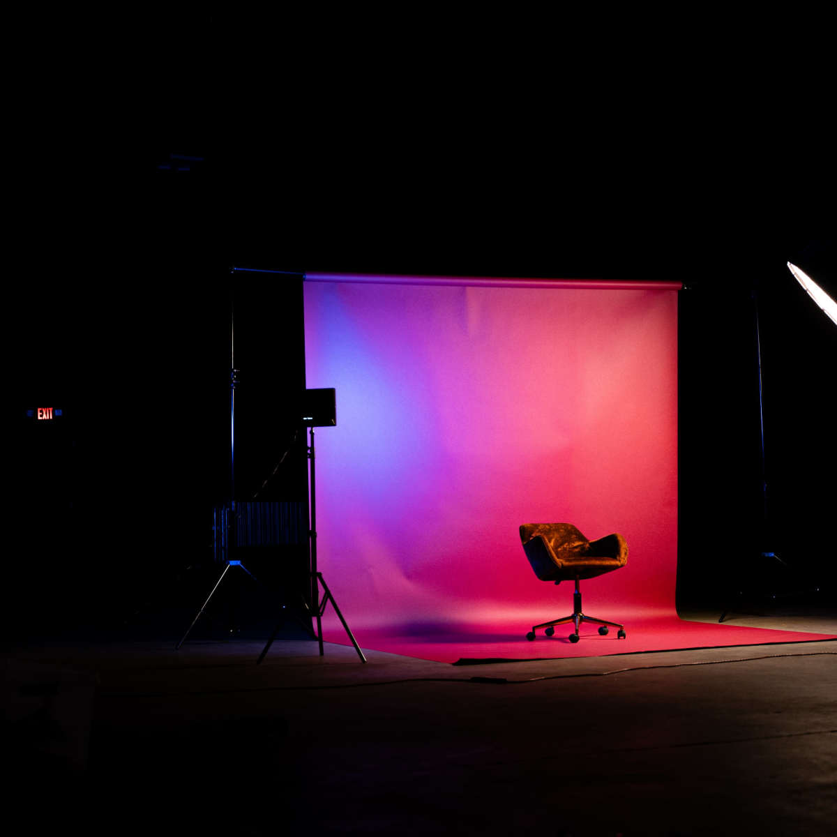 A single chair is positioned in front of a gradient backdrop illuminated by soft lighting in a dark studio.
