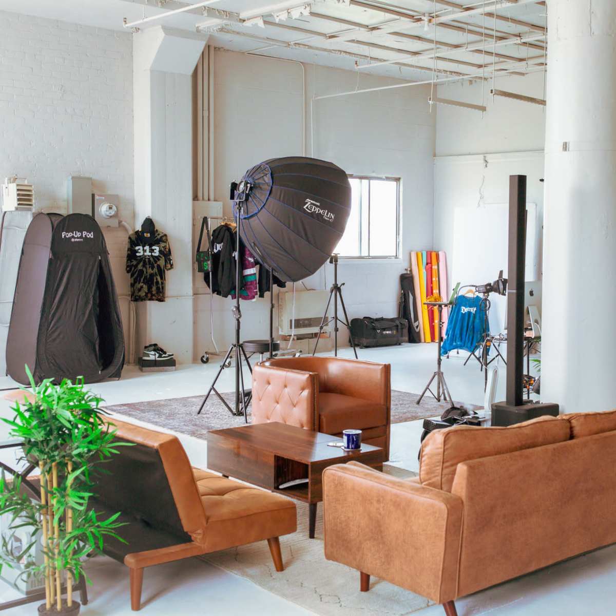A spacious studio with a brown couch, a coffee table, and photography equipment set up around the room, including softbox lights and backdrops.