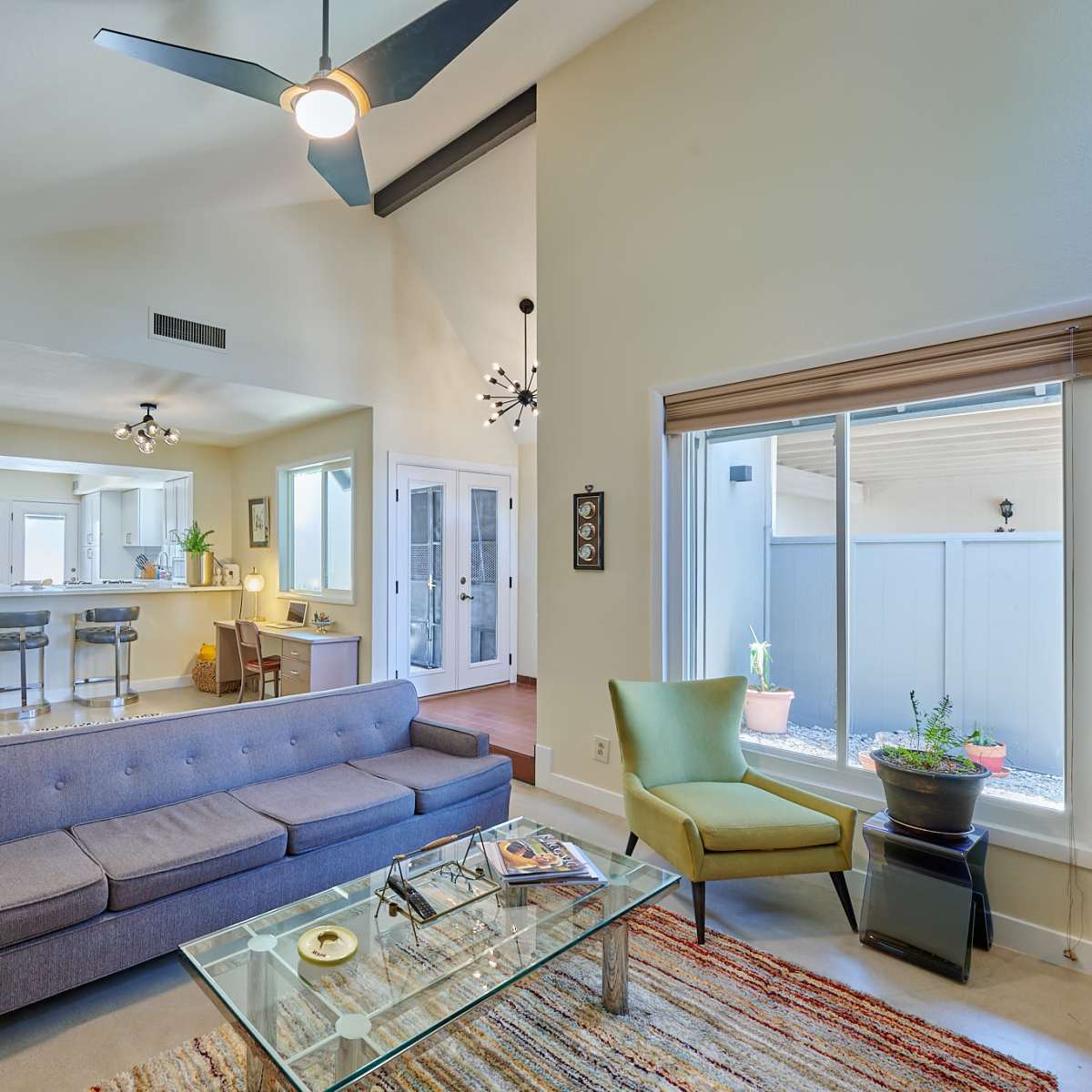 A modern living room with a gray sofa, a glass coffee table, and large windows that allow natural light to enter.