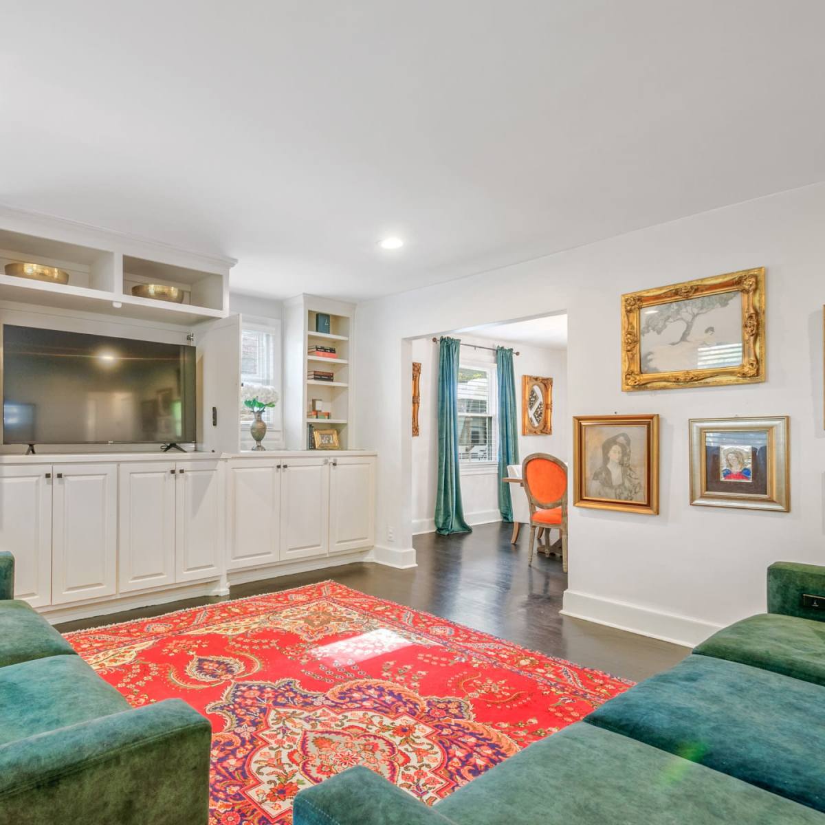 A living room features a green sectional sofa, a red patterned rug, and a built-in cabinet housing a television.