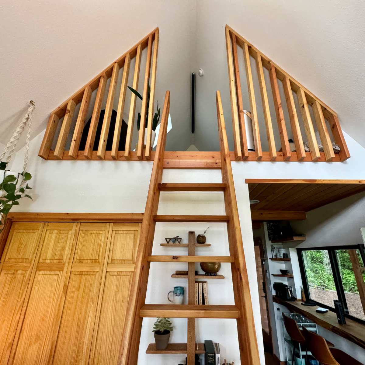 A wooden ladder leading to a loft area with railings, surrounded by white walls and wooden cabinetry in an open-concept space.
