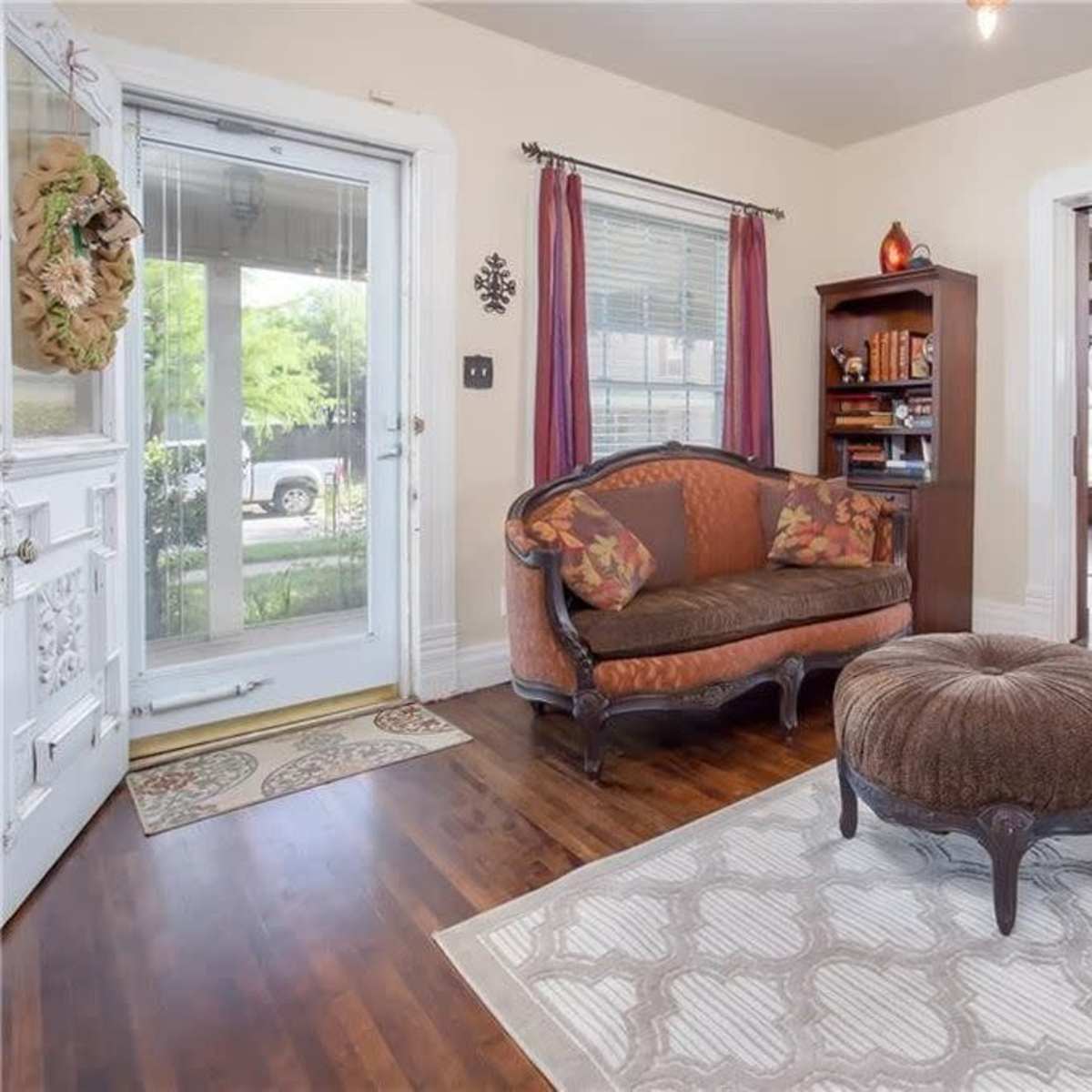 A cozy living area featuring a decorative couch, a round ottoman, and an open doorway leading to a dining space with wooden furniture.