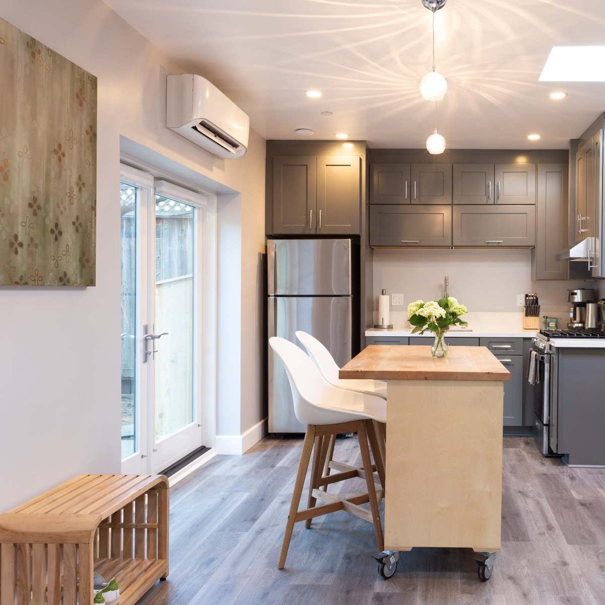 A modern kitchen and living area featuring gray cabinetry, a central island with seating, and large windows allowing natural light.