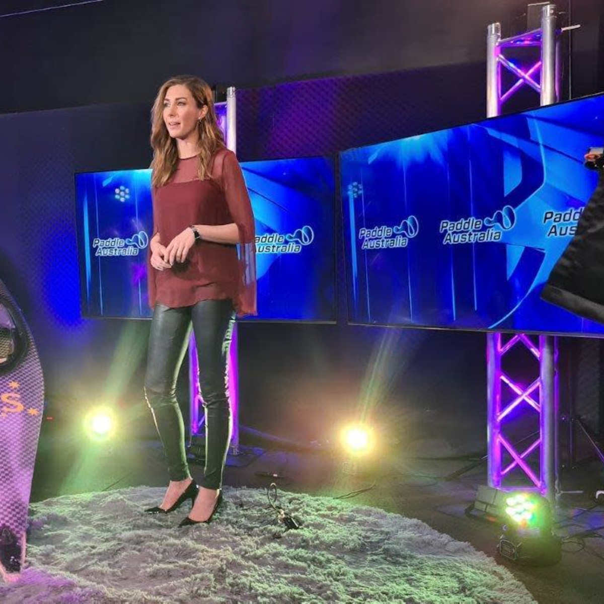 A presenter stands on a stage with multiple screens displaying "Paddle Australia" and a kayak nearby.