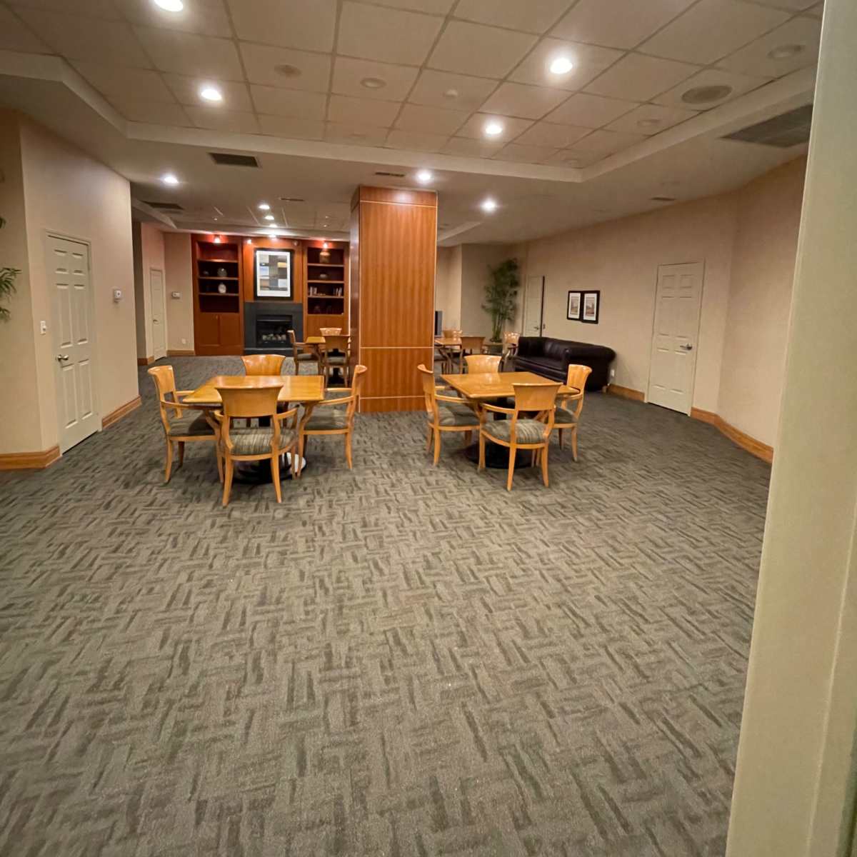 A well-lit, empty room featuring several wooden tables and chairs arranged around a central area.
