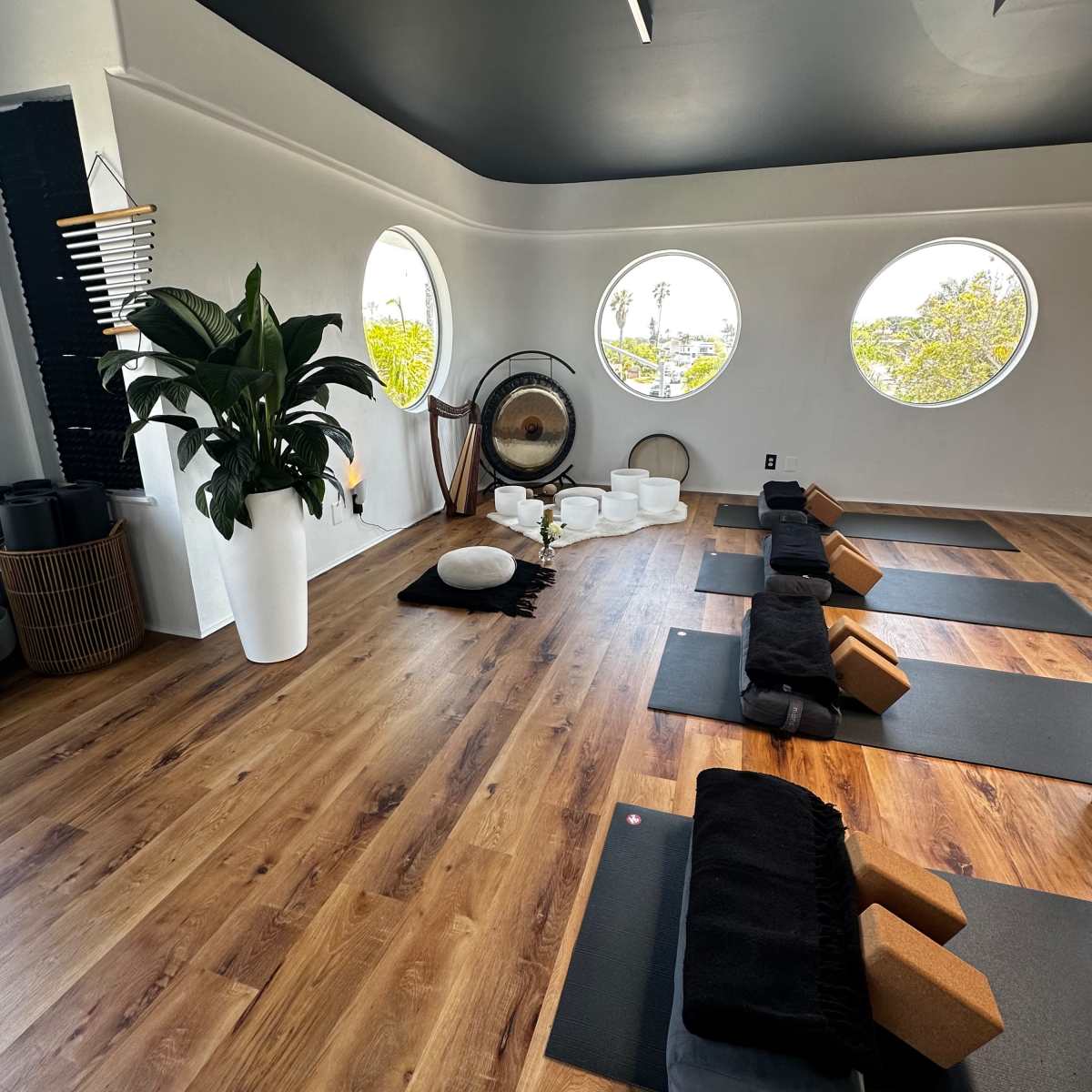 A serene yoga studio with circular windows, wooden flooring, and neatly arranged yoga mats and props.