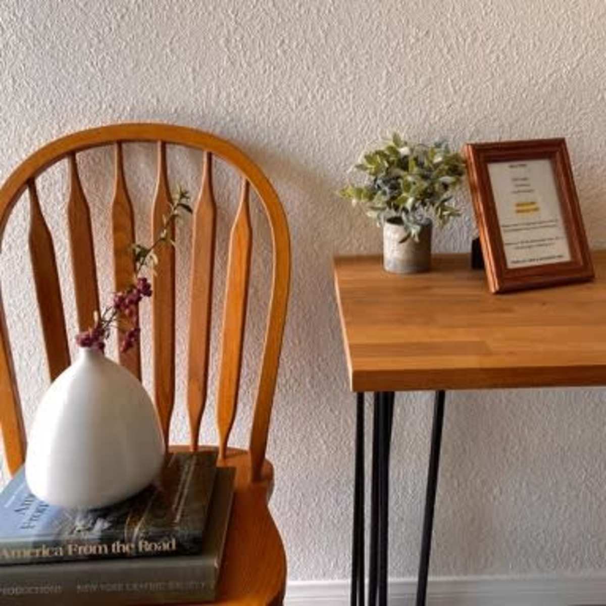 A wooden chair with a vase of flowers sits next to a small table displaying a framed certificate and a decorative plant.