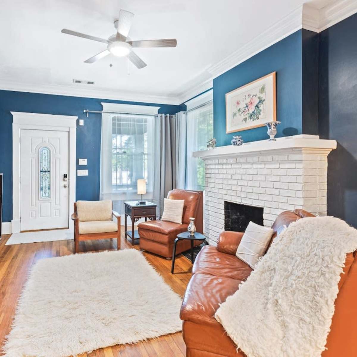 A living room with a blue accent wall, a white brick fireplace, two brown leather chairs, and a small rug on the wooden floor.