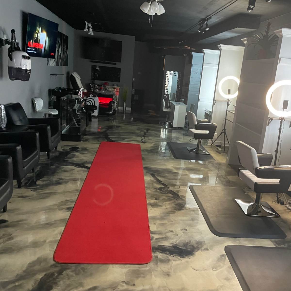 A modern salon interior with black leather chairs, styling stations, a red carpet, and ring lights, illuminated by soft overhead lighting.