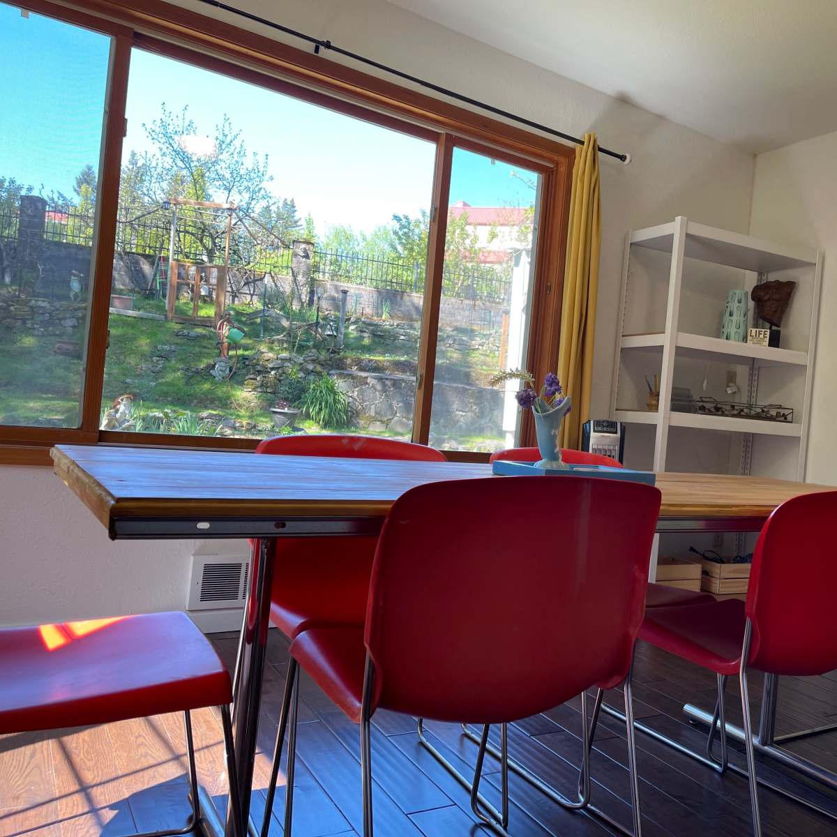 A modern meeting room features a wooden table surrounded by red chairs, with a large window overlooking a landscaped garden.