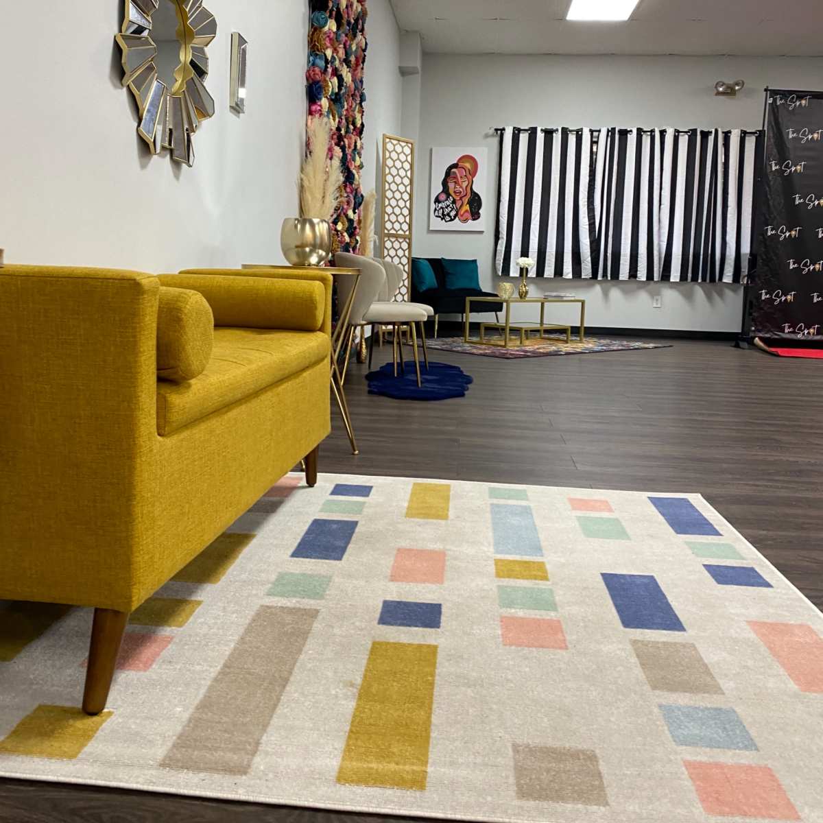 A modern interior space featuring a yellow couch, a patterned area rug, and various decorative elements on the walls, including artwork and mirrors.