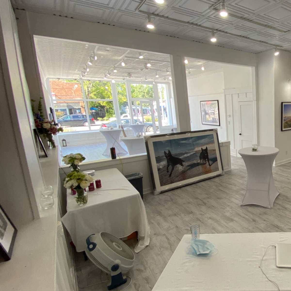 An art gallery featuring white tables, framed photographs on the walls, and a view of windows letting in natural light.