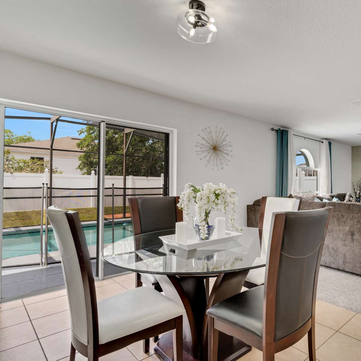 A modern living space featuring a dining area with a round table and chairs, an adjacent living area with a sofa, and large windows overlooking a pool.