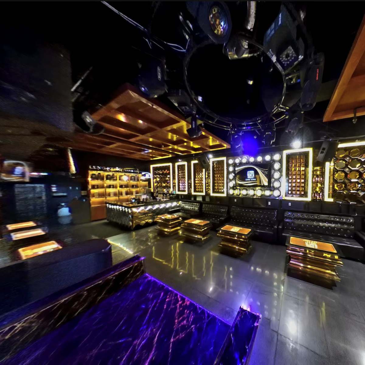 An upscale lounge with leather seating, illuminated decor, and a bar area featuring shelves of bottles.