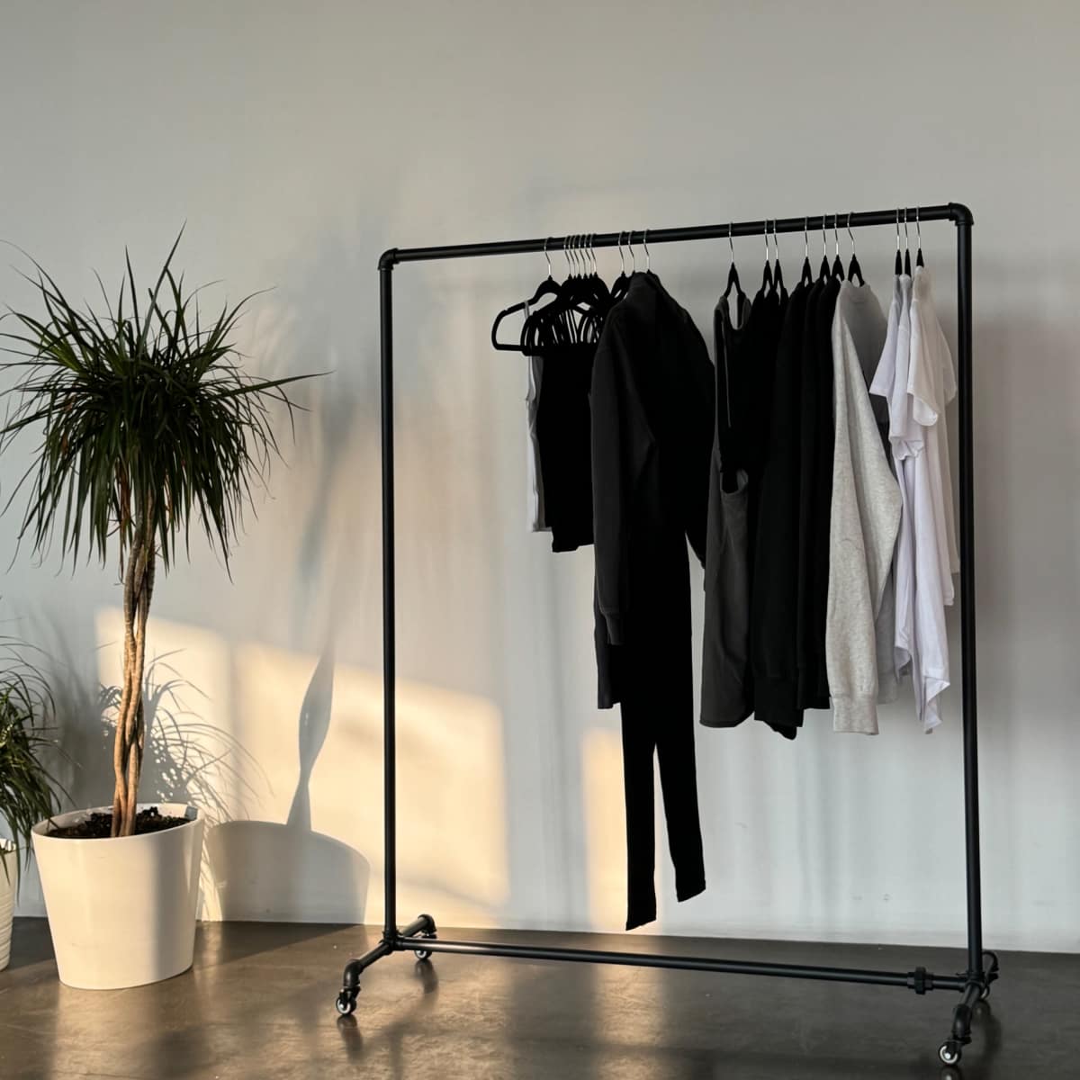 A clothing rack with a variety of garments hangs beside a potted plant in a minimalist interior space.