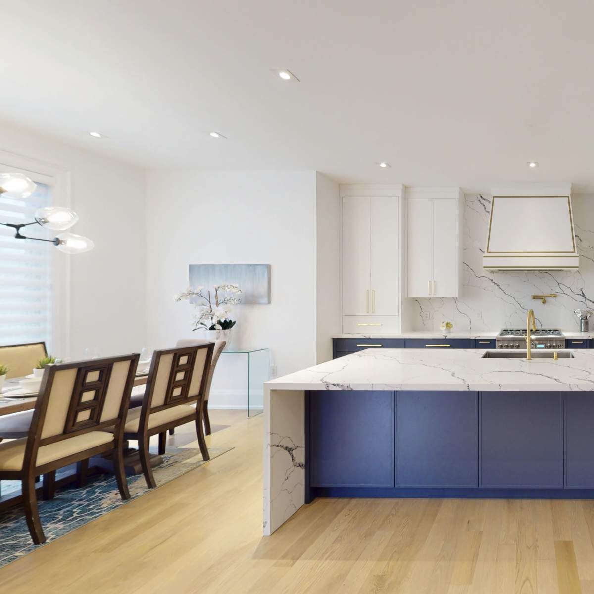 A modern kitchen features a large marble island with a blue base, white cabinetry, and stainless steel appliances.