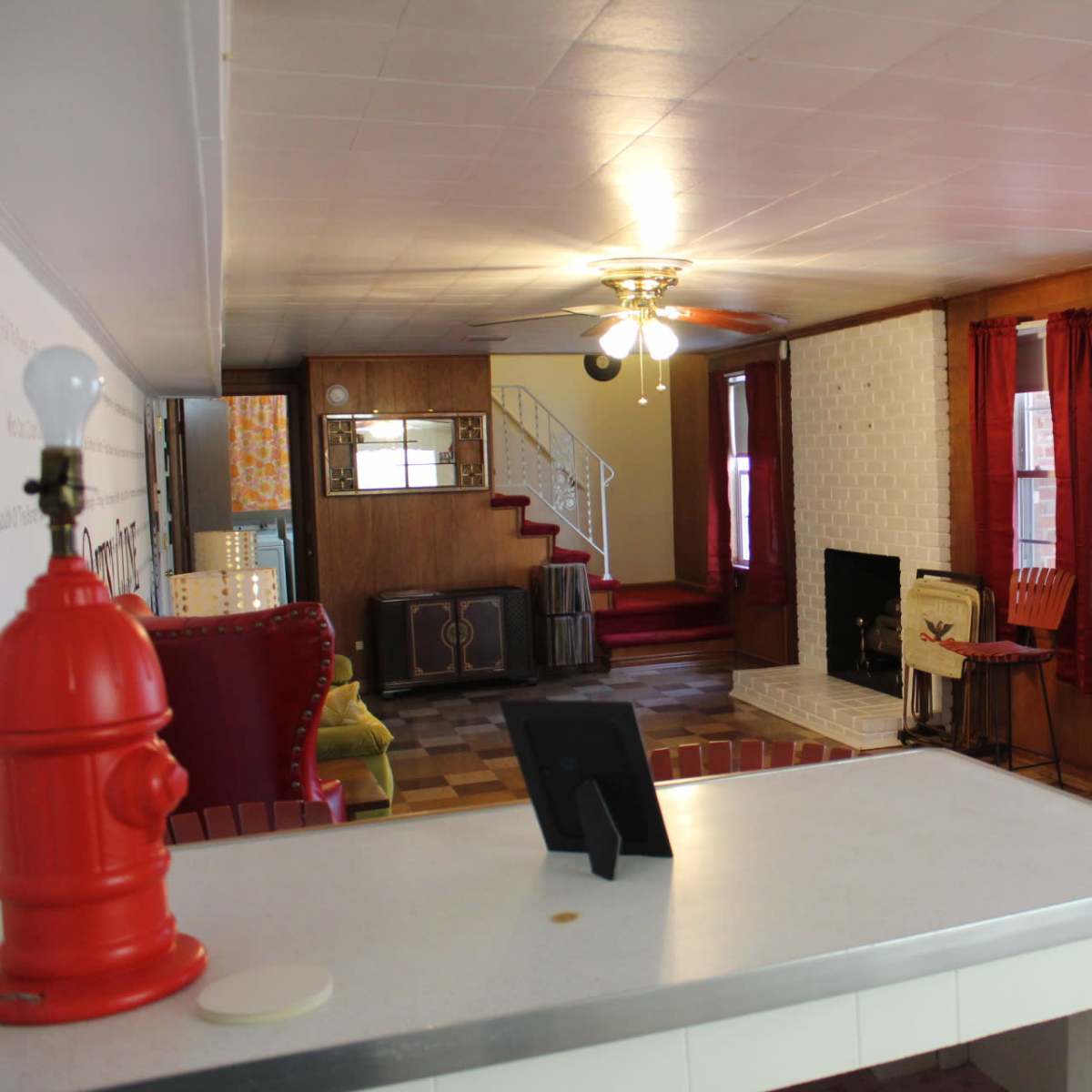 A living room with a fireplace, red curtains, and a sliding glass door leading to an outdoor area, along with a kitchen bar in the foreground.
