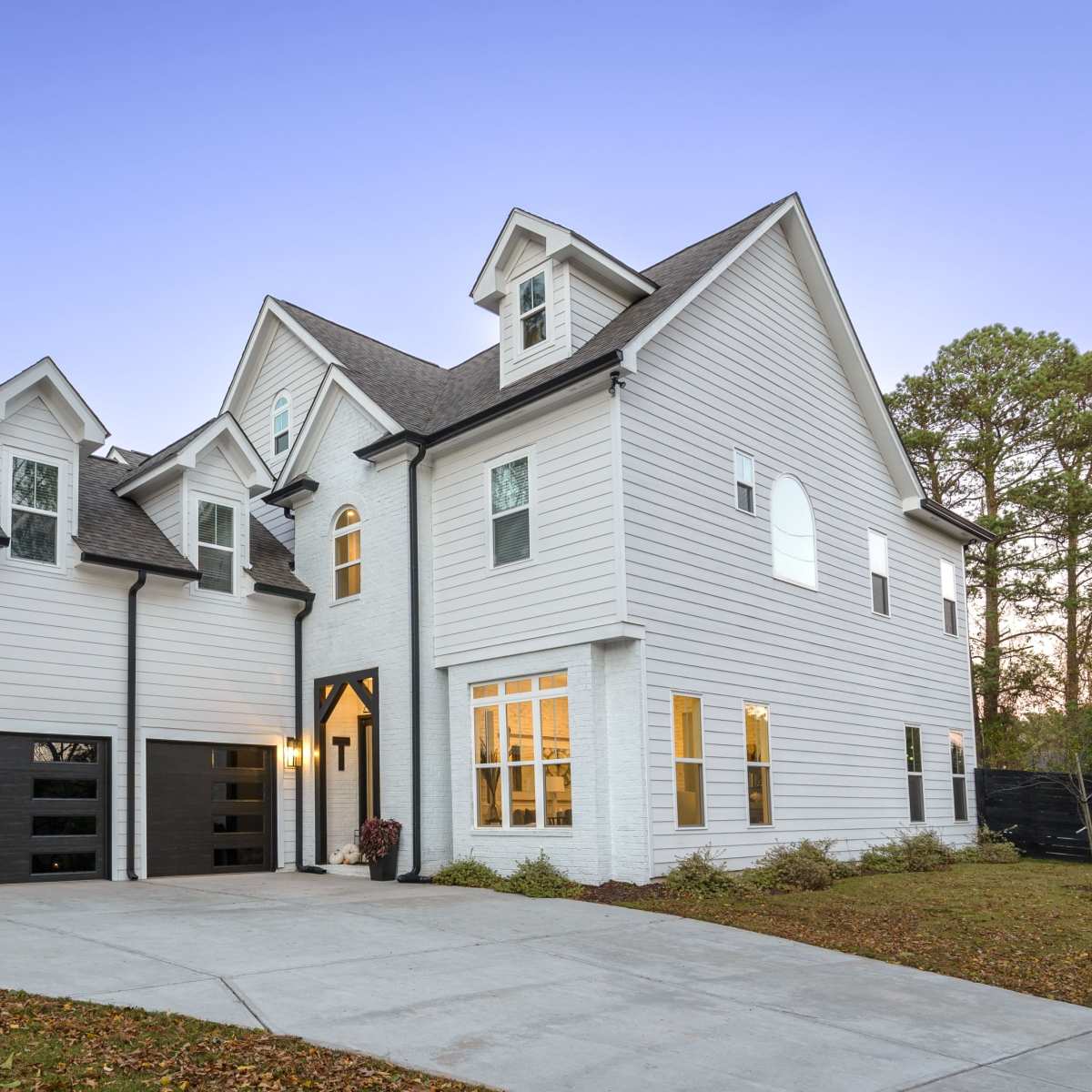 A modern two-story white house with black accents and a basketball hoop in the driveway.
