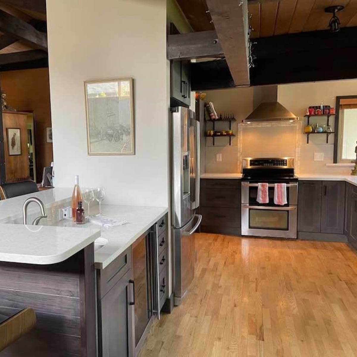 A modern kitchen with a large island featuring a sink and bar seating, open to a dining area with wooden beams and a contemporary layout.