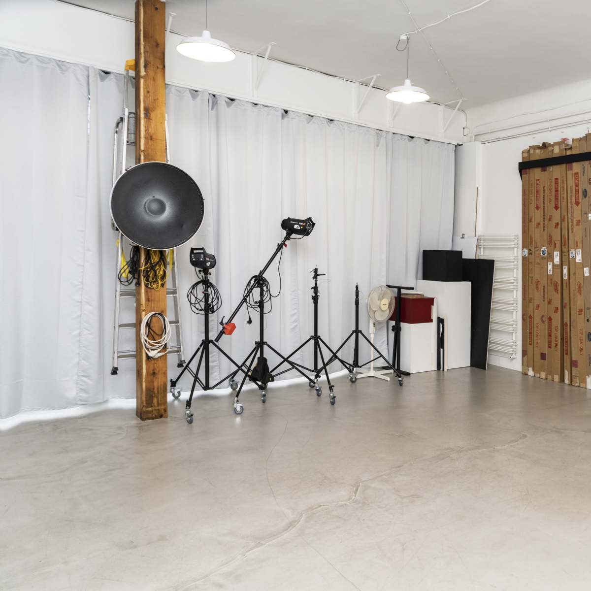 A photography studio with various lighting equipment, tripods, and a backdrop against a white wall.