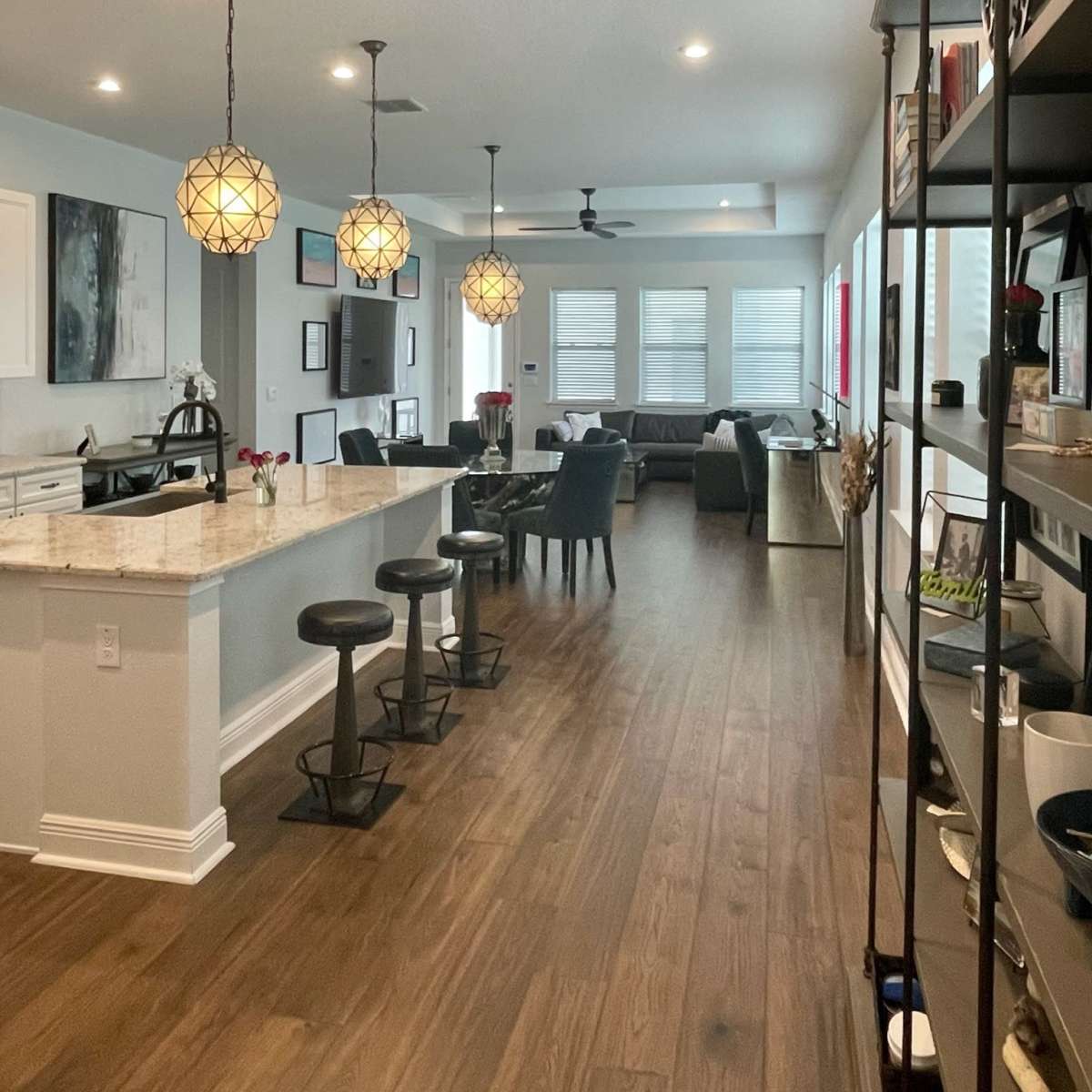 A modern open-concept kitchen and living area with a long island bar, three pendant lights, and a view of a seating area.