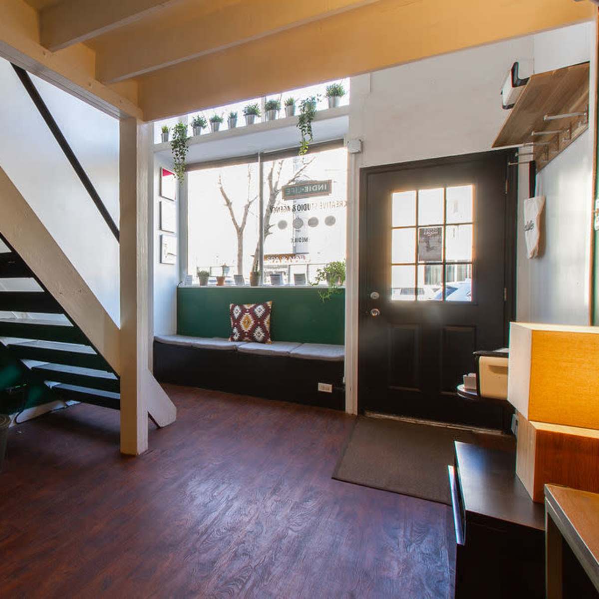 A small interior space with a staircase on the left, a water cooler, a bench by the window, and a black door leading outdoors.