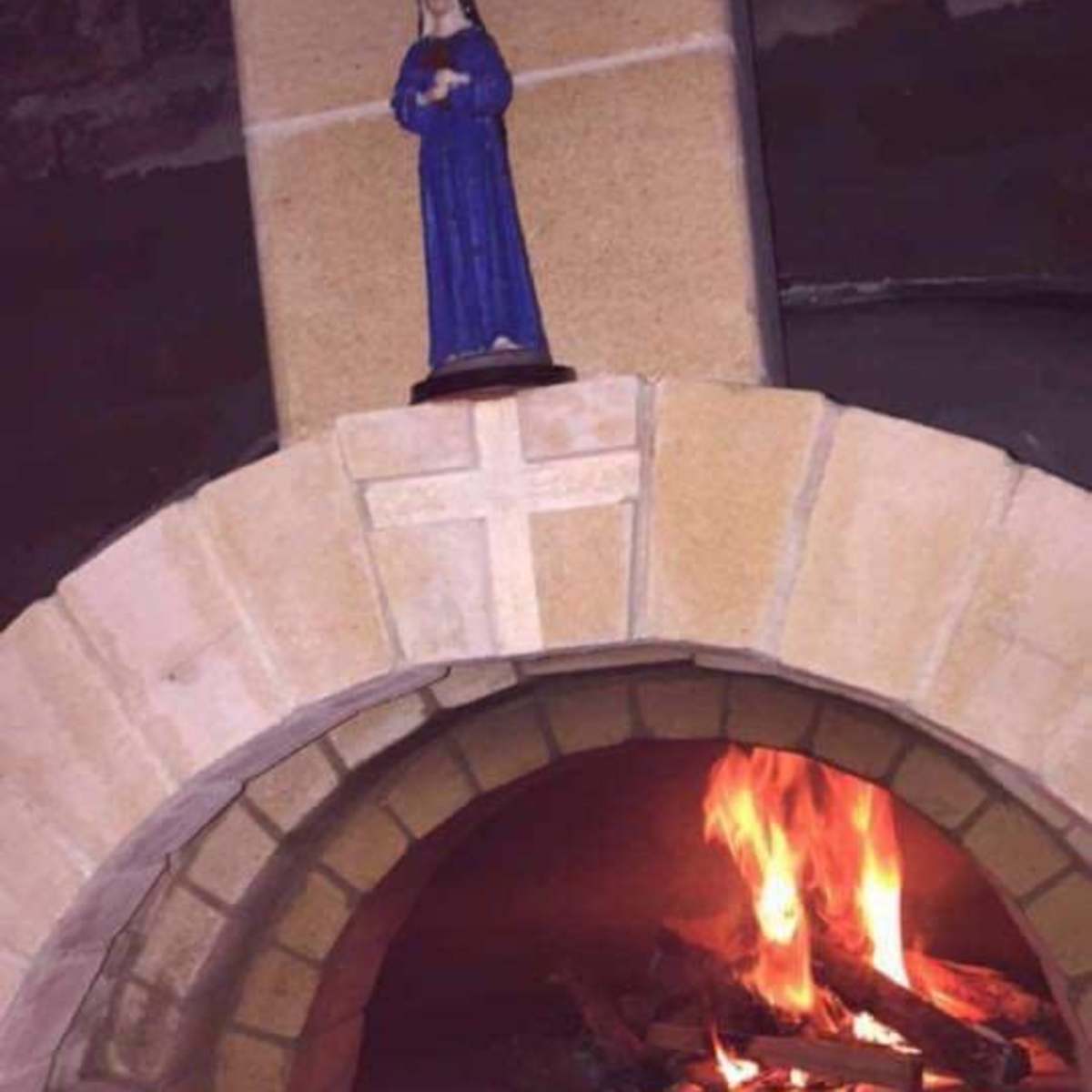 A brick fireplace with a figurine of a woman on top and a fire burning inside.