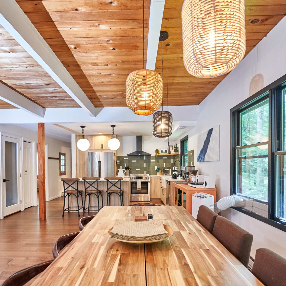 A modern dining area featuring a wooden table with eight chairs, pendant lighting, and an open kitchen in the background.