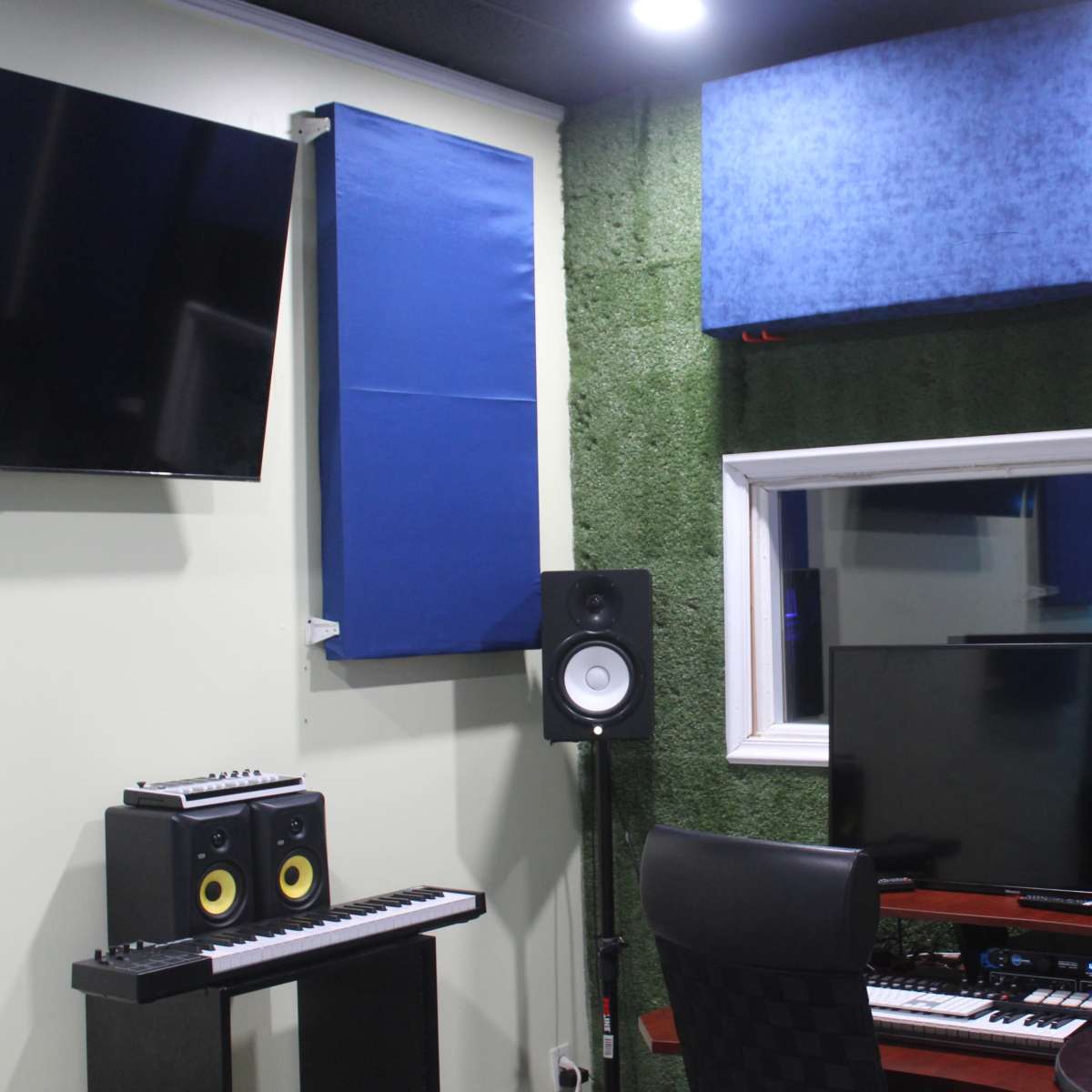 A recording studio with soundproofing panels on the walls, a monitor, speakers, and a keyboard setup.