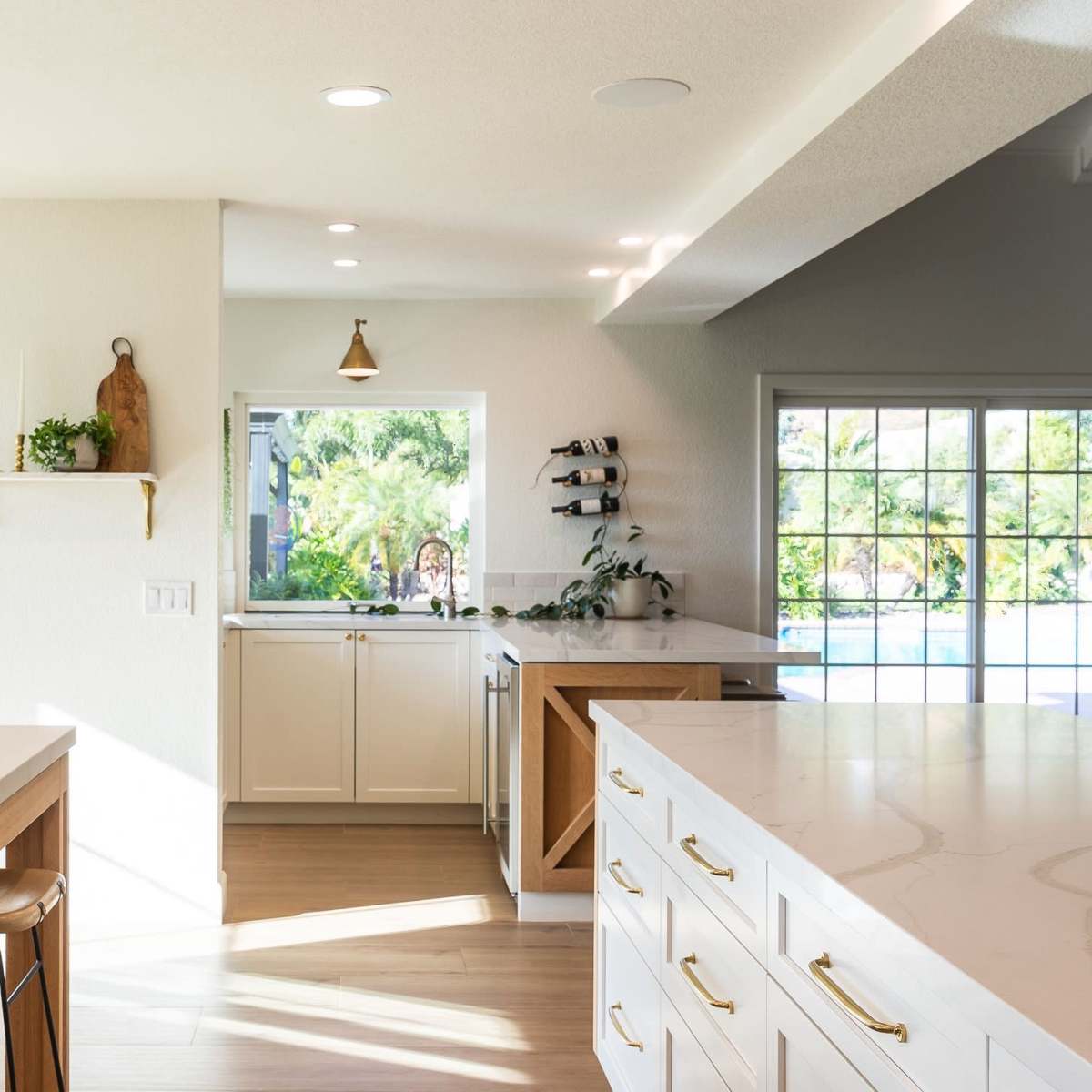 A modern kitchen features white cabinetry, large countertops, and a view of an outdoor pool area through expansive windows.