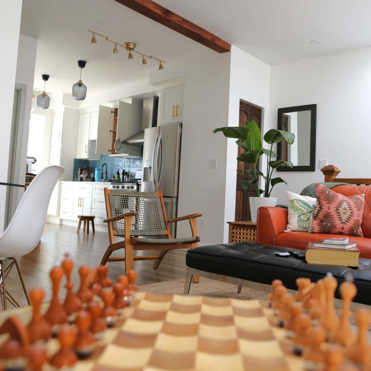 A modern living space with a chess set on a table, a leather sofa, and a kitchen area in the background.