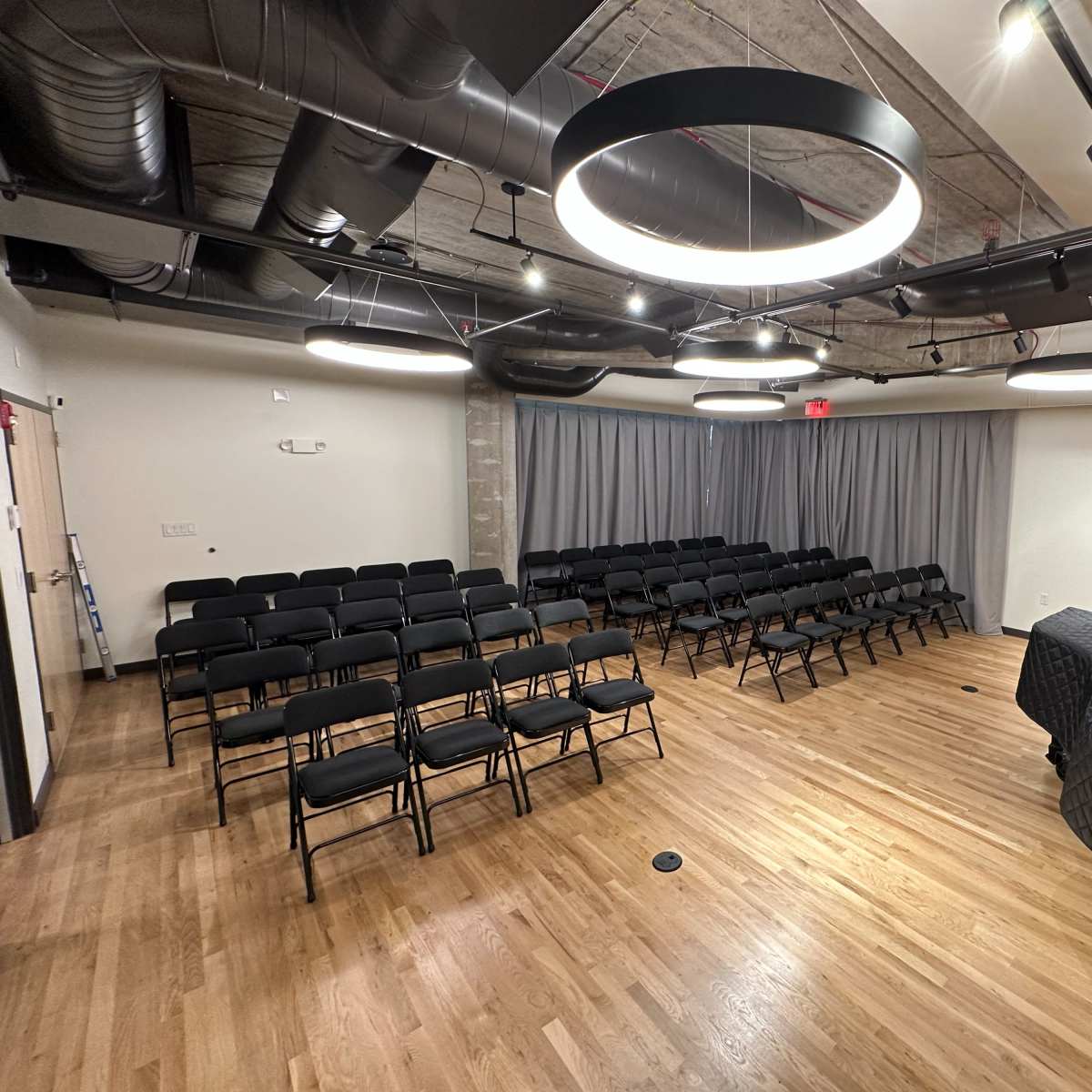 A newly designed meeting room with rows of black chairs facing a stage, equipped with modern lighting and wooden wall panels.