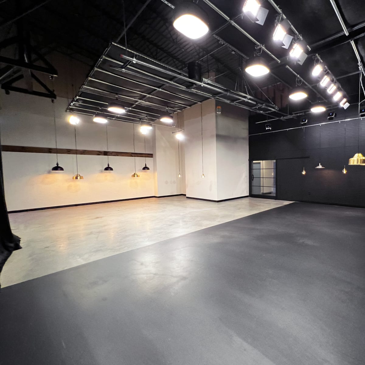 A spacious interior studio with black flooring, bright overhead lights, and pendant lights hanging from the ceiling.