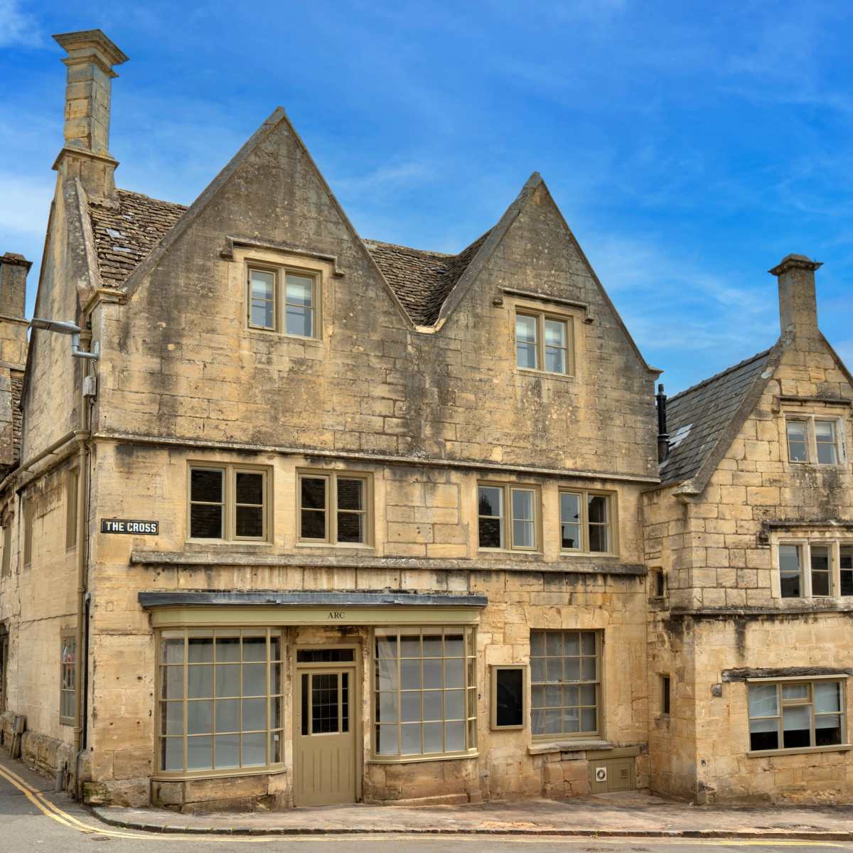 Two stone buildings with steep roofs, situated on a quiet street under a blue sky.