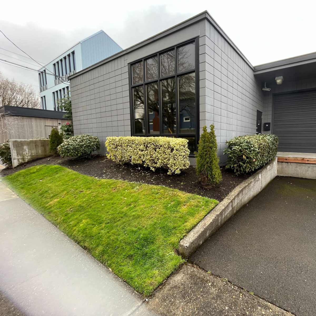 A modern gray building with a landscaped front yard, featuring a driveway and a garage door.