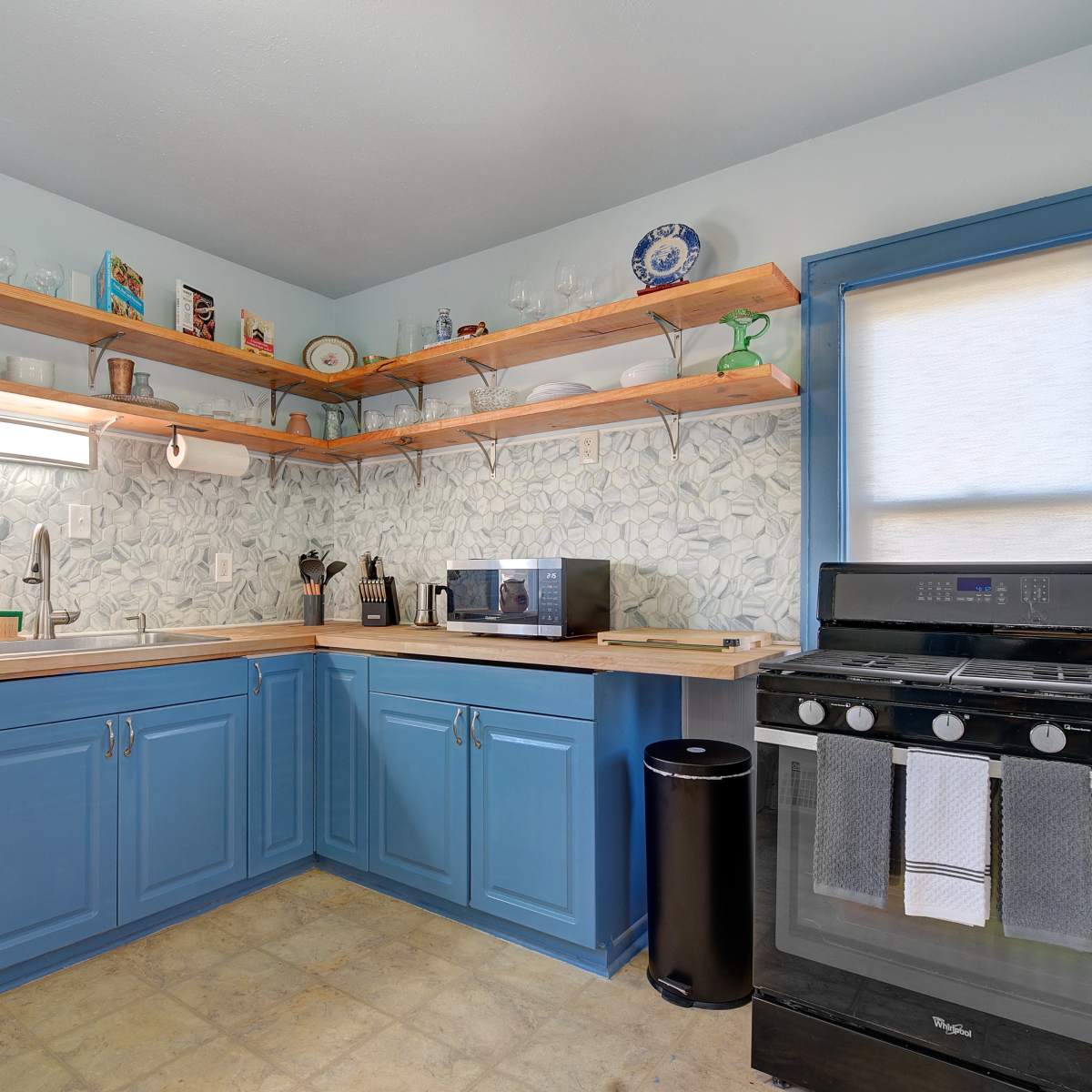 A modern kitchen features blue cabinetry, wooden shelves, and appliances including a microwave and stove.