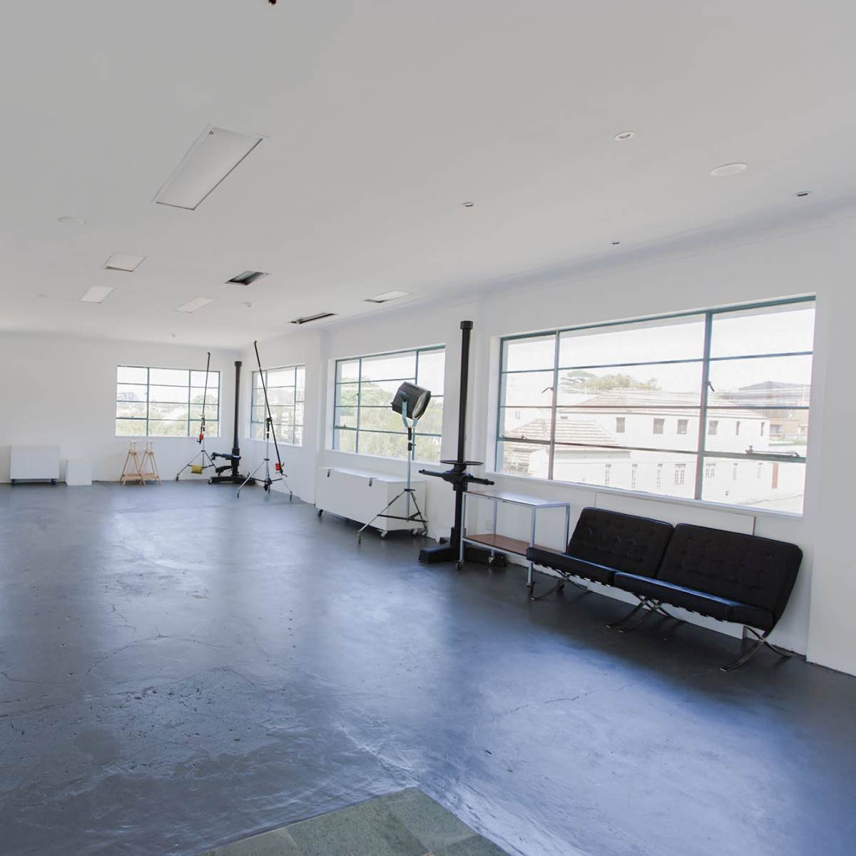 A spacious, empty studio with large windows, minimal furniture, and a polished concrete floor.