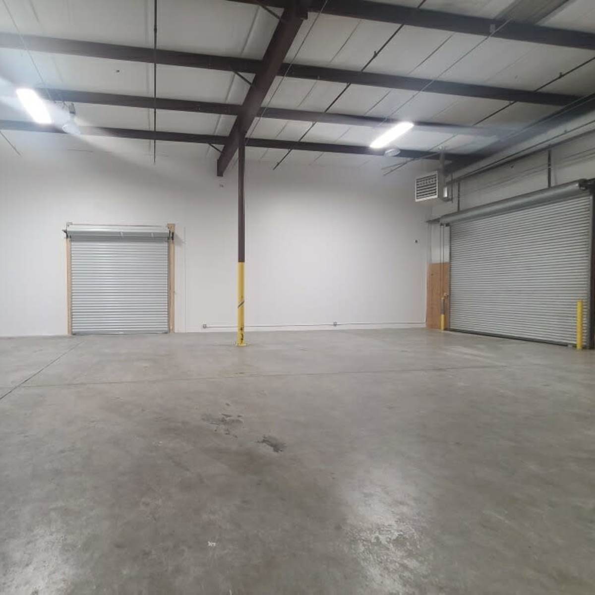 An empty industrial warehouse with concrete flooring and two roll-up doors on opposite walls.