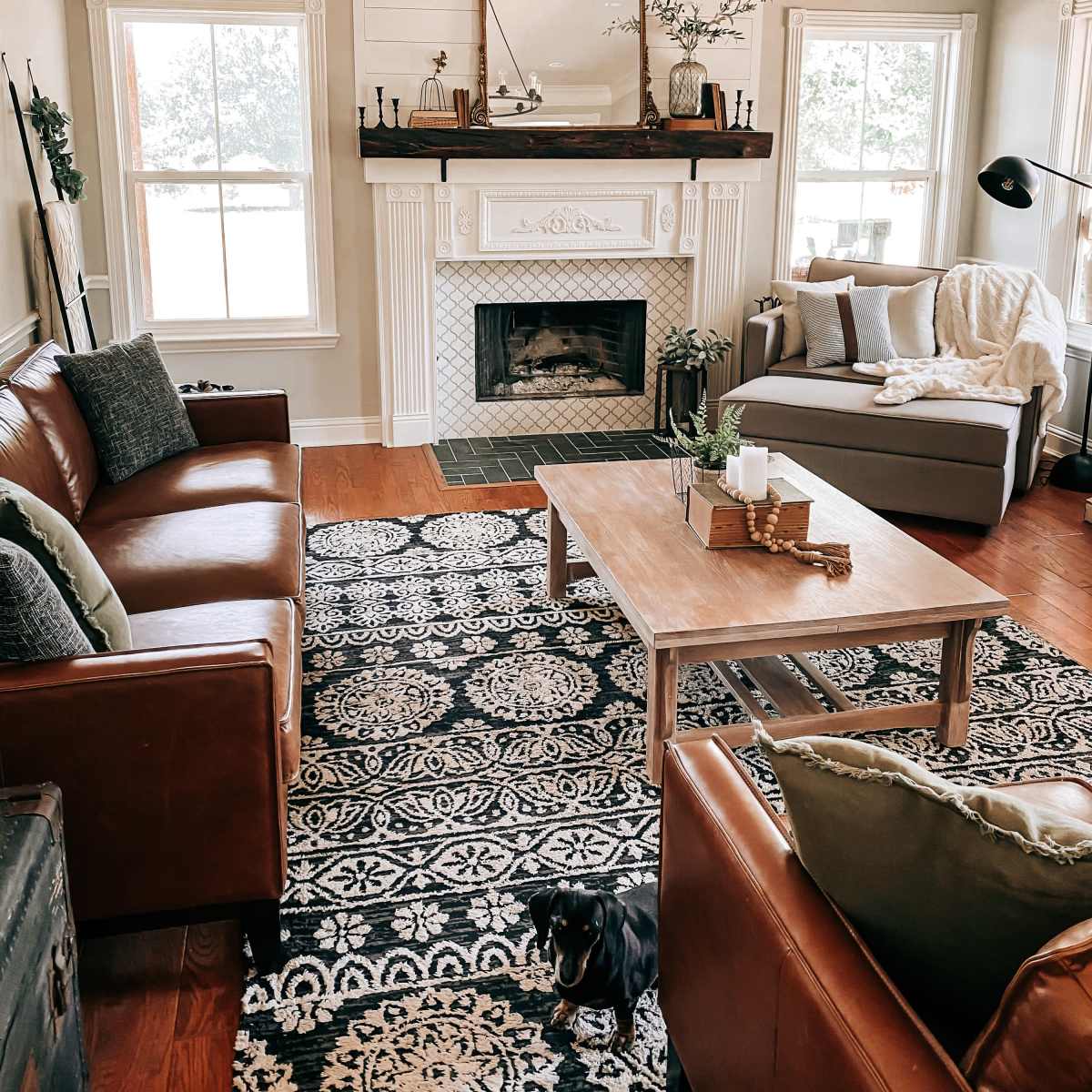 A cozy living room featuring two brown leather sofas, a wooden coffee table, and a fireplace with a decorative mirror above it, all set against a patterned rug.