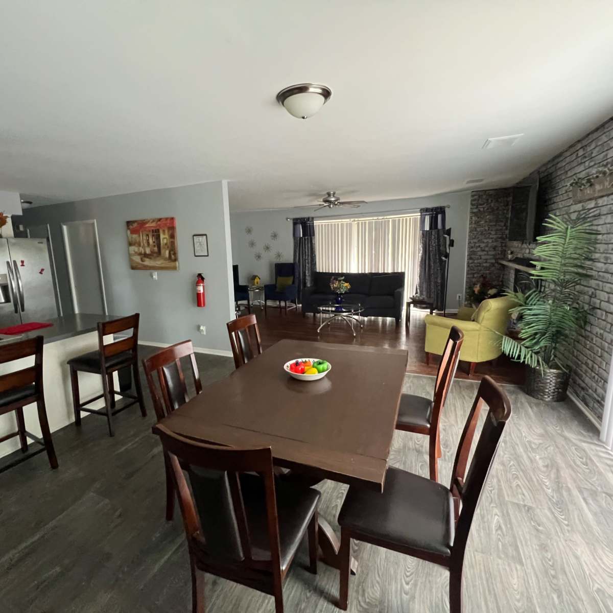 A dining area with a rectangular table and eight chairs is visible, leading to a living space with a black couch and a green chair.