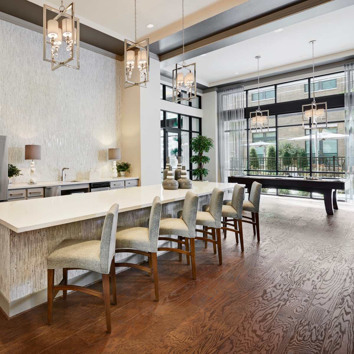 A modern kitchen area with a long countertop, several bar stools, and large windows that allow natural light to fill the space.
