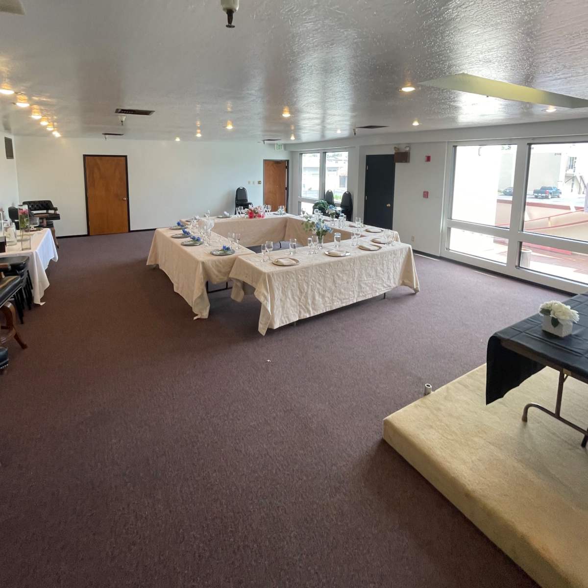 A spacious event room with a central arrangement of dining tables covered in white tablecloths and surrounded by chairs.