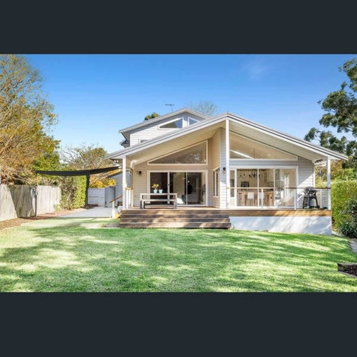 A modern two-story house with a large deck overlooks a neatly maintained lawn and garden.
