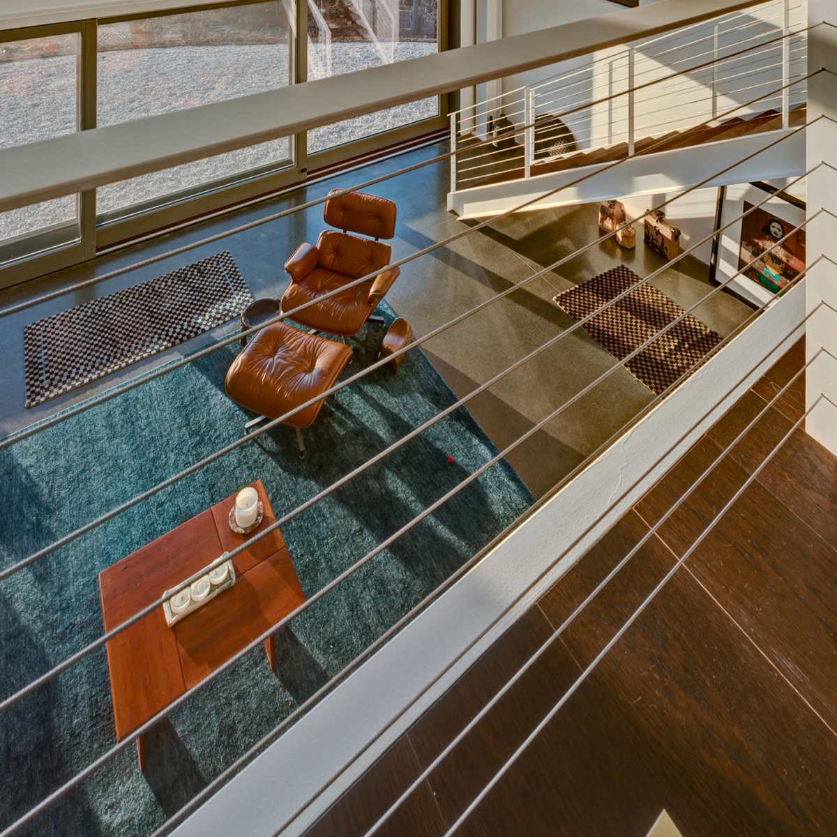 A modern living space with large windows overlooking a body of water, featuring a lounge chair and a coffee table on a patterned rug.