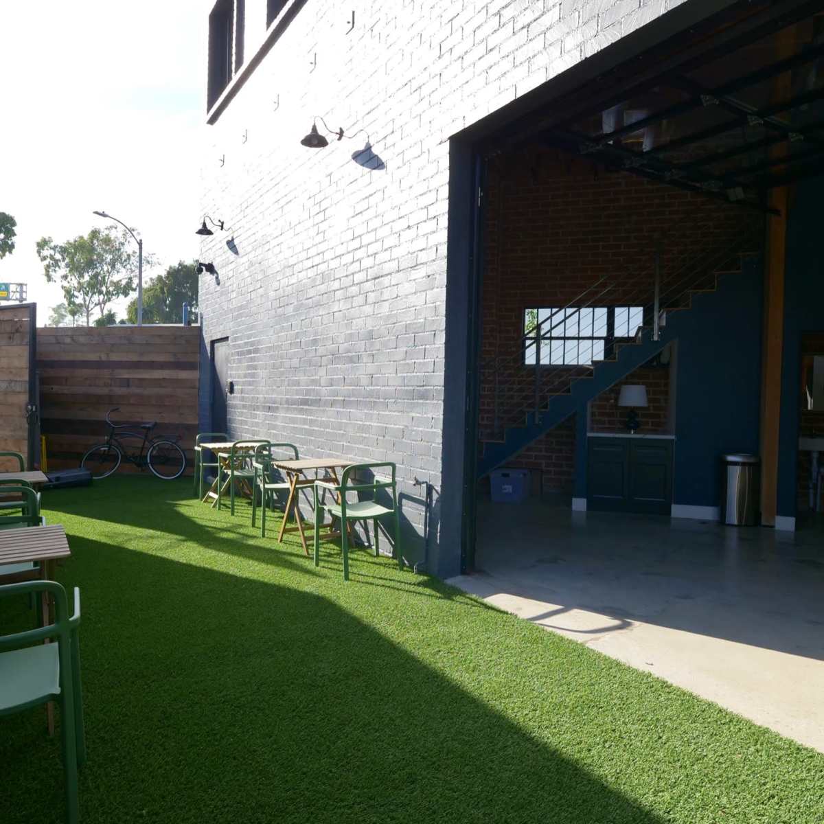 An outdoor seating area with green chairs and wooden tables adjacent to a modern building with a partially open garage door.