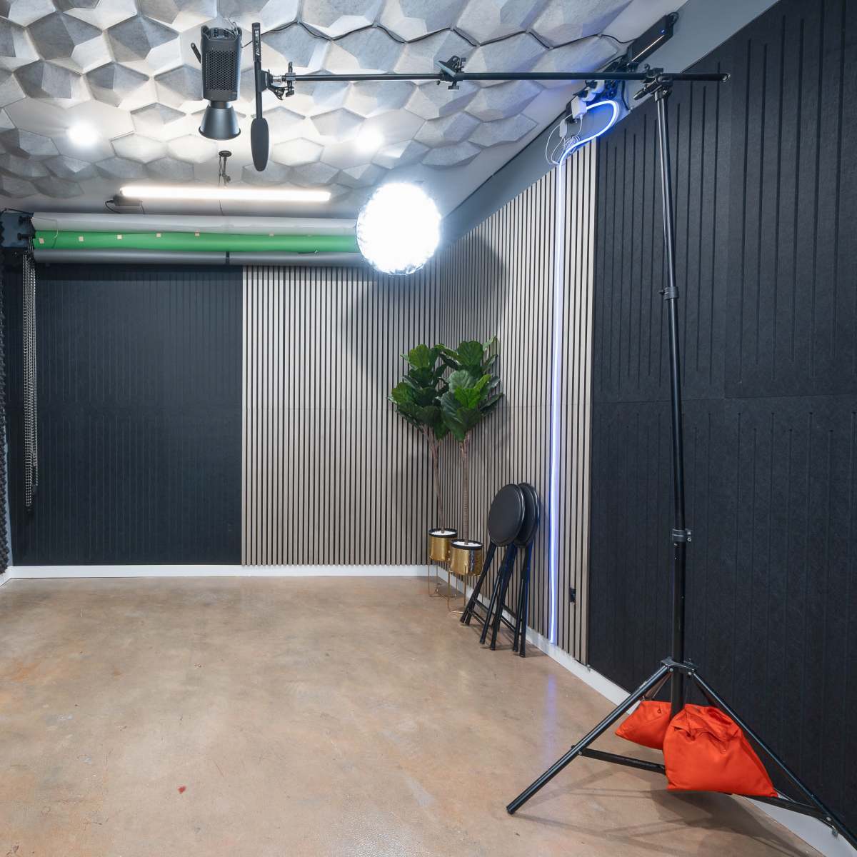A vacant studio space with acoustic wall panels, a mounted light, and a television on a black table.