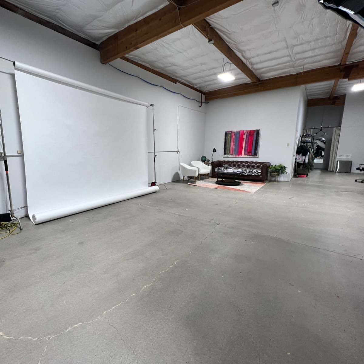 A spacious studio with a roll-up backdrop, a brown leather couch, and minimal furnishings on a concrete floor.