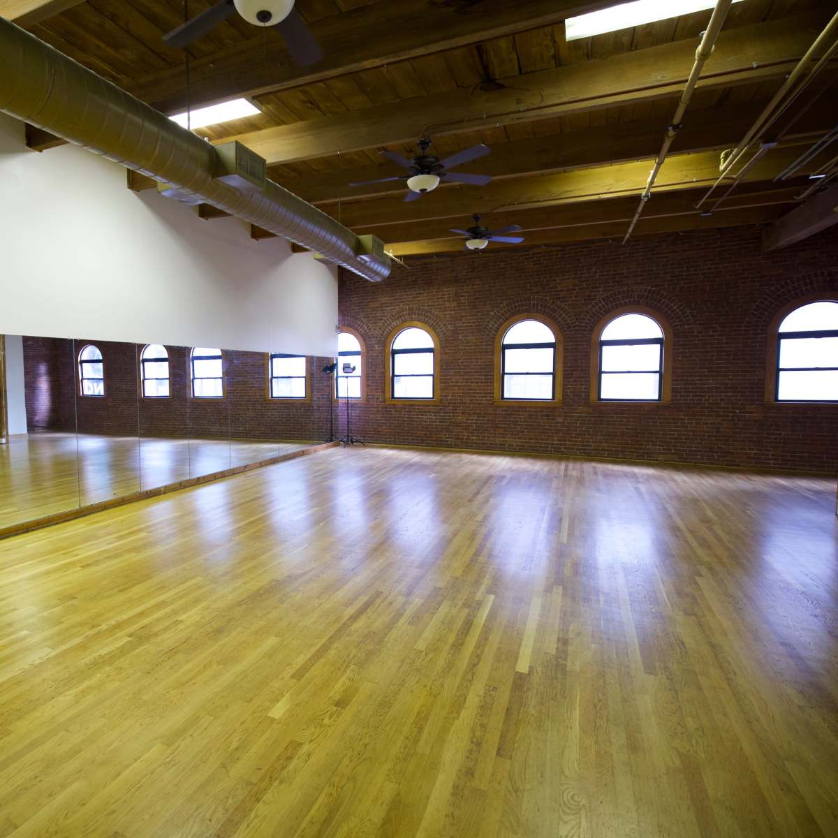 A spacious wooden-floored room with large windows and a wall of mirrors.