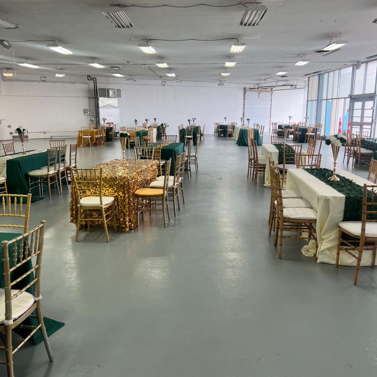 A large, empty indoor space set up with gold and green tablecloths and chairs arranged for an event.